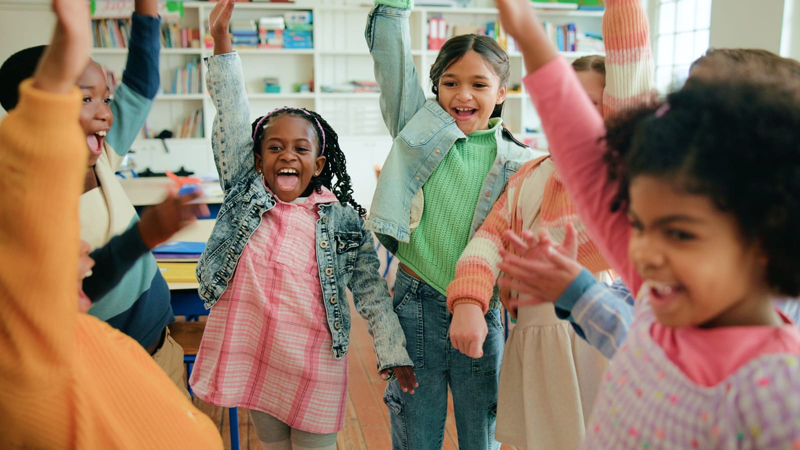 Primary-school children cheering with their hands in the air in a classroom