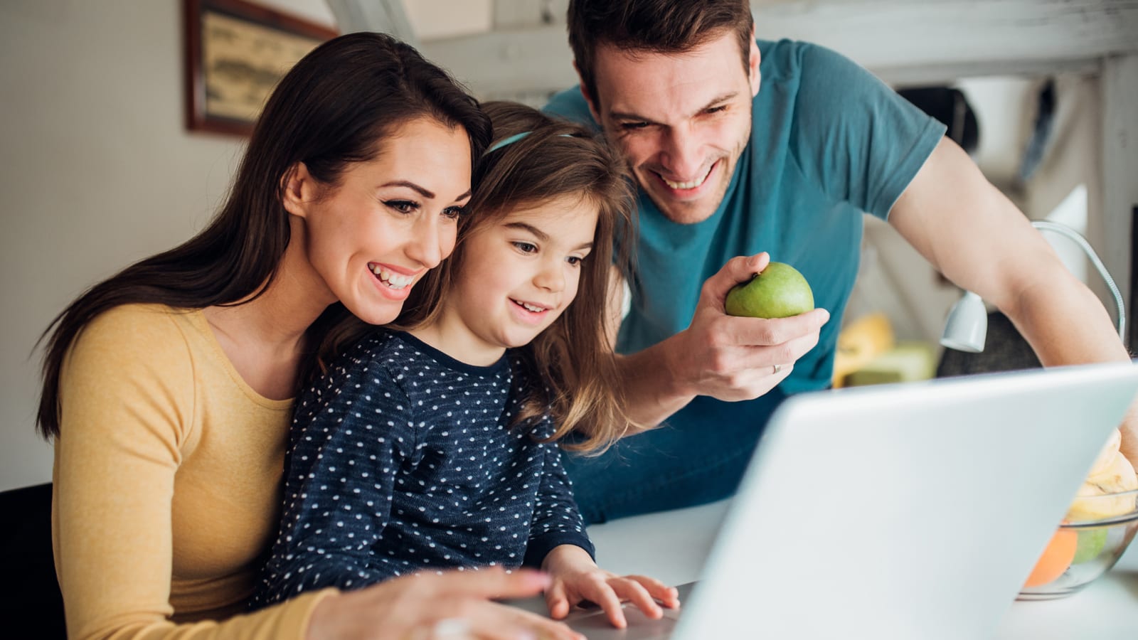 A mother, father and young daughter looking at a laptop together at home